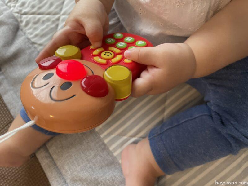 アンパンマンごきげんメロディリモコンを両手でもつ0歳女の子